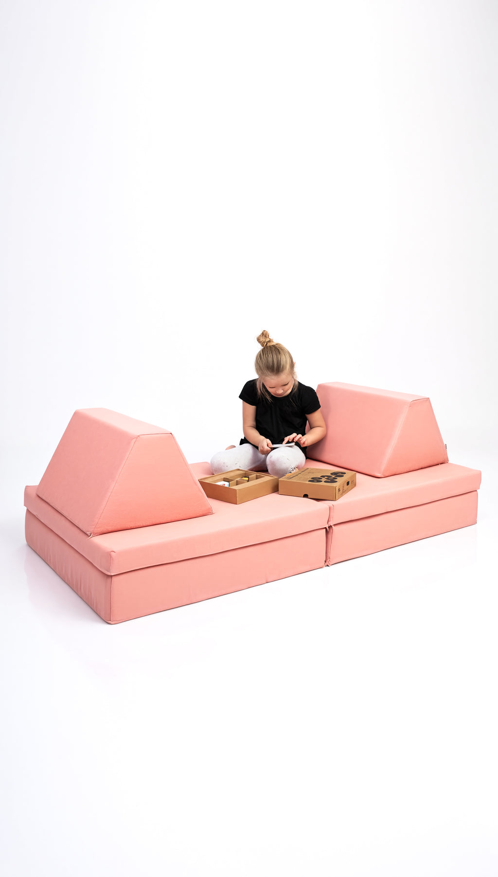 Person sitting on a pink modular sofa with two wooden baskets on a white background