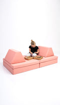 Person sitting on a pink modular sofa with two wooden baskets on a white background