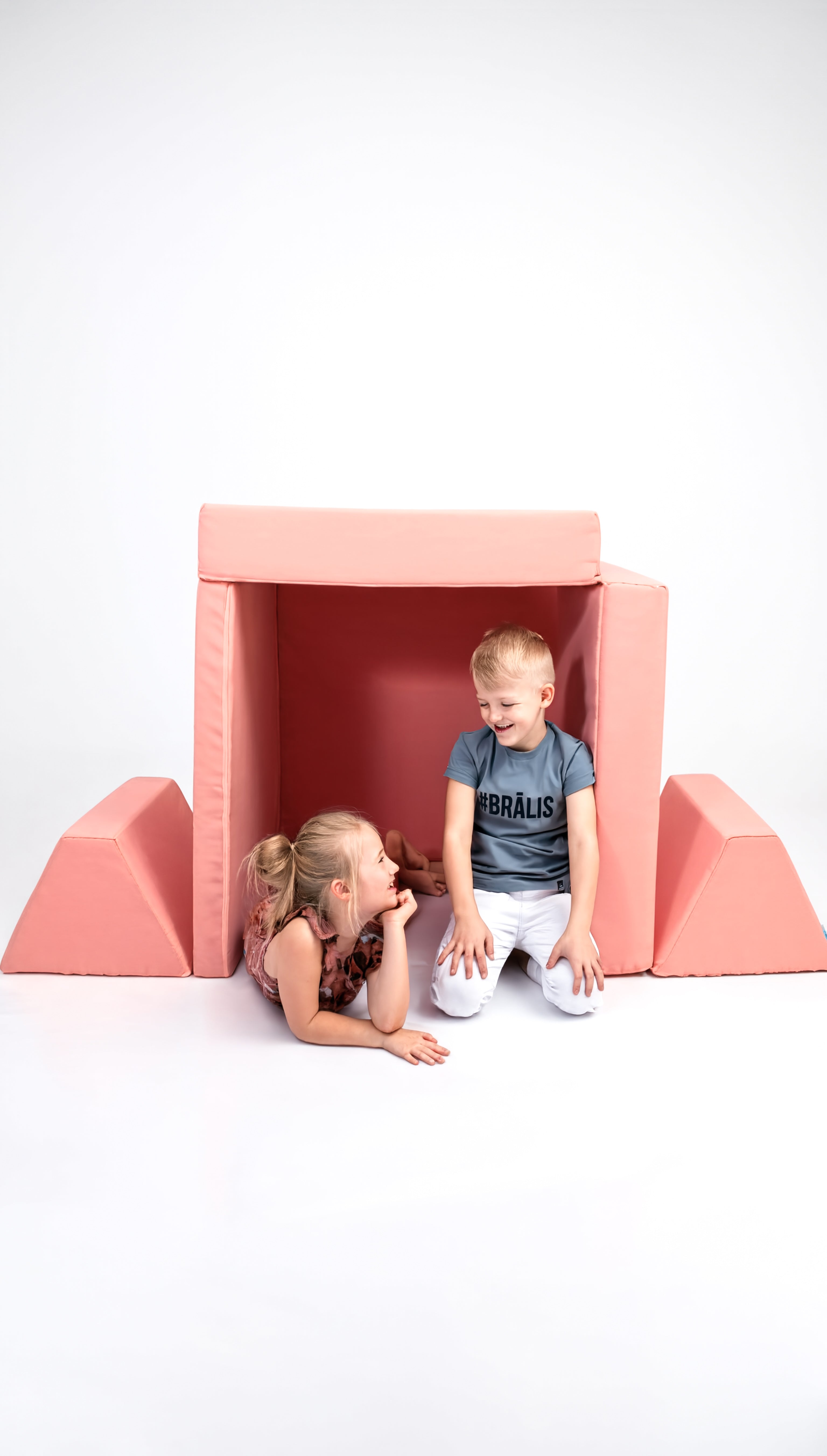 Two children sitting inside a pink playhouse on a white background