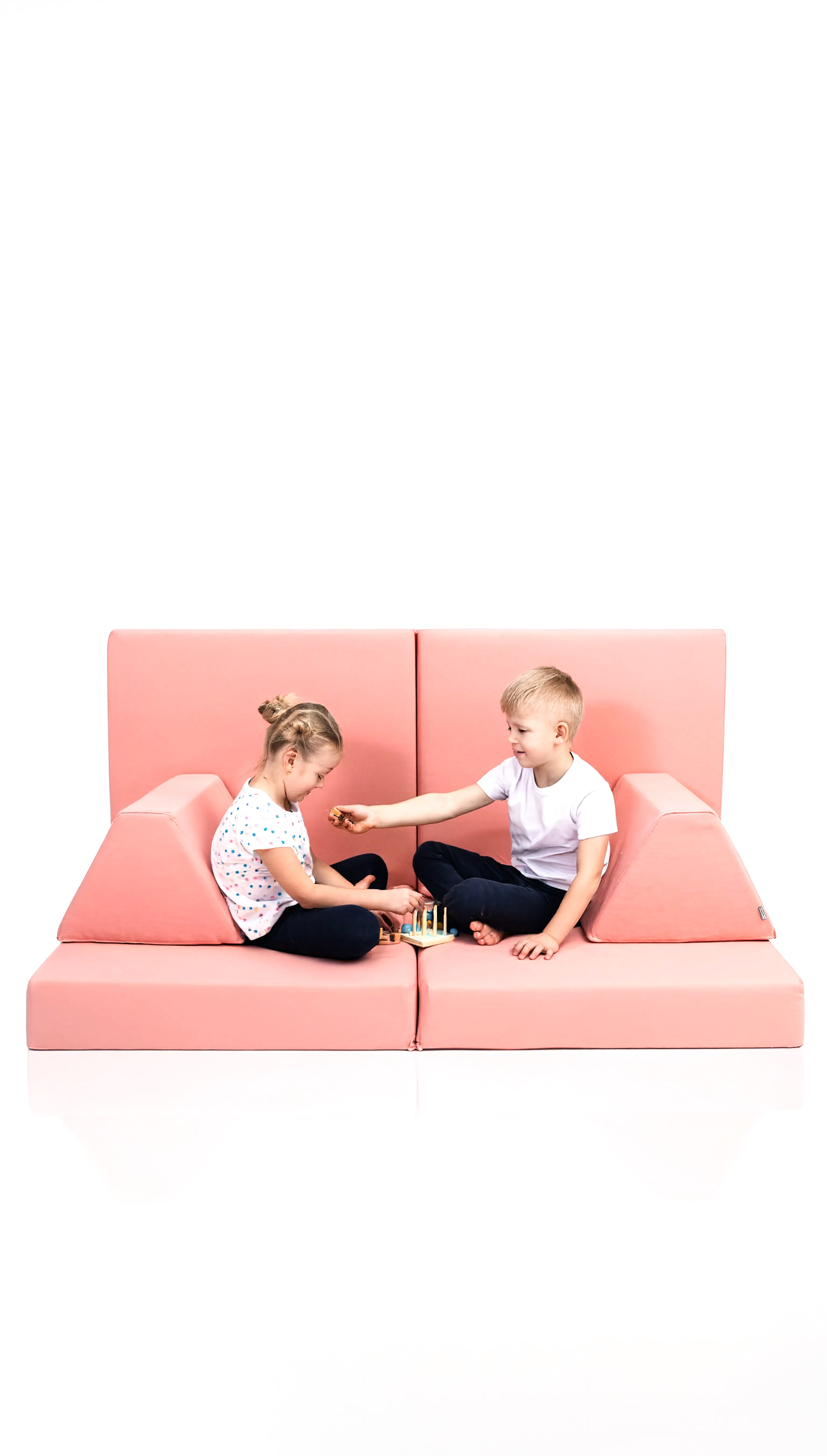 Two children sitting on a pink sectional sofa against a white background