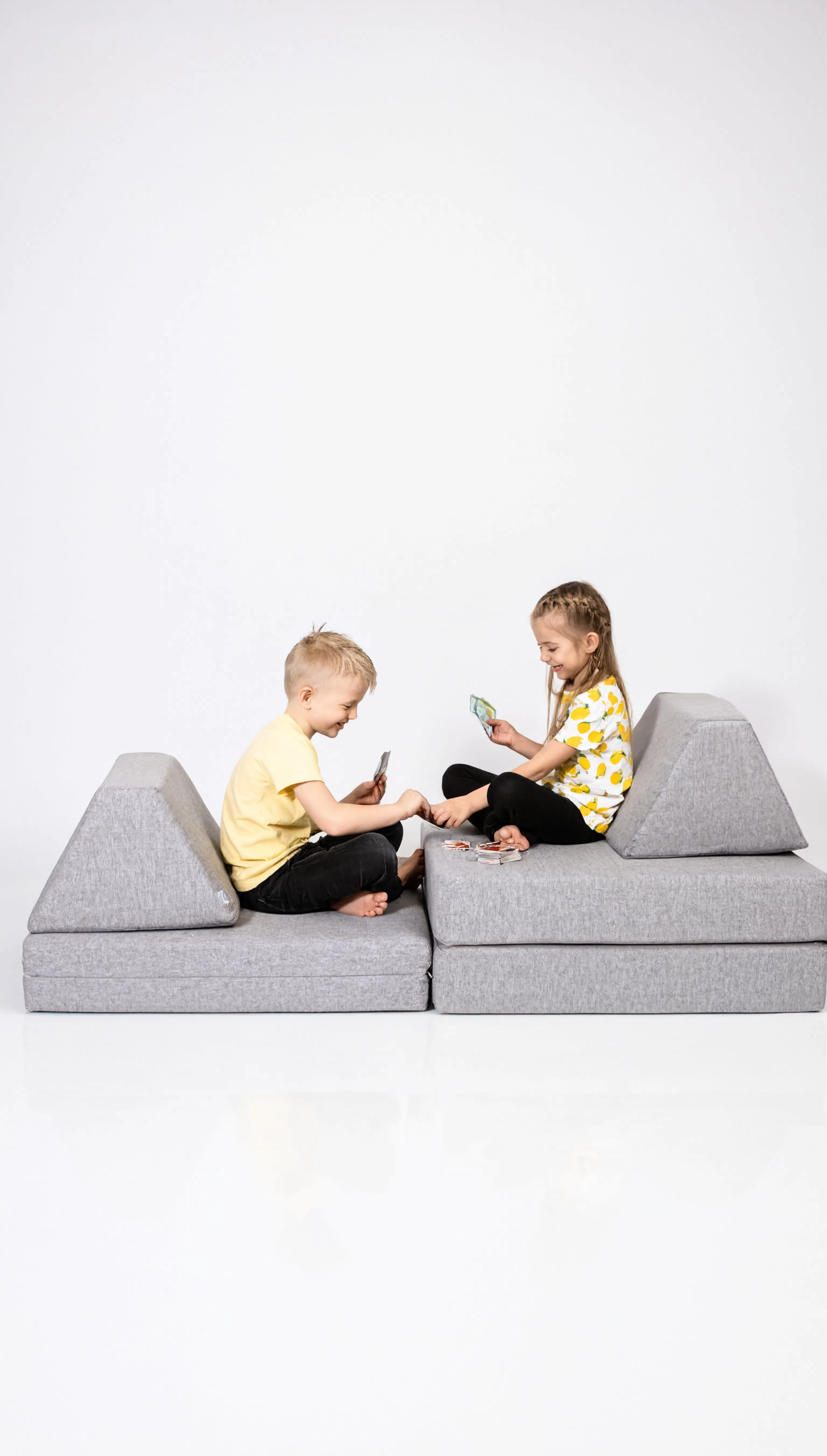 Two children sitting on a modern gray sofa with a white background
