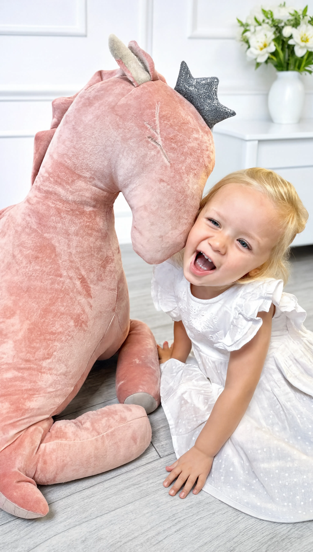 Child playing with a large pink plush toy in a room with white walls and decor.