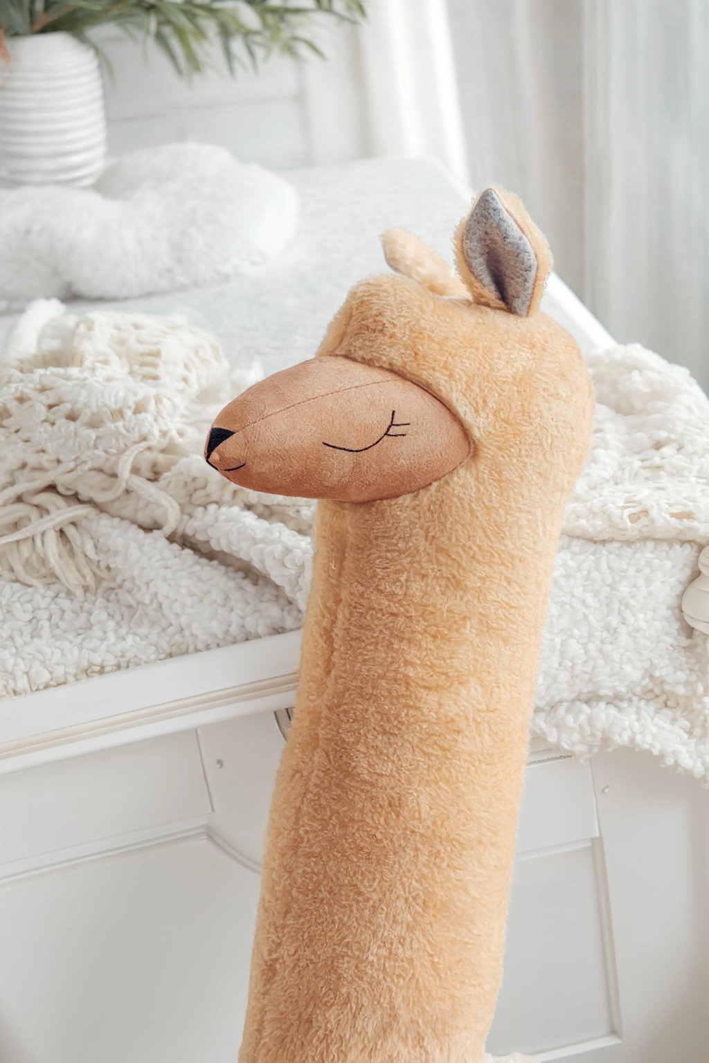 Plush deer toy on a white surface with a soft blanket and plant in the background