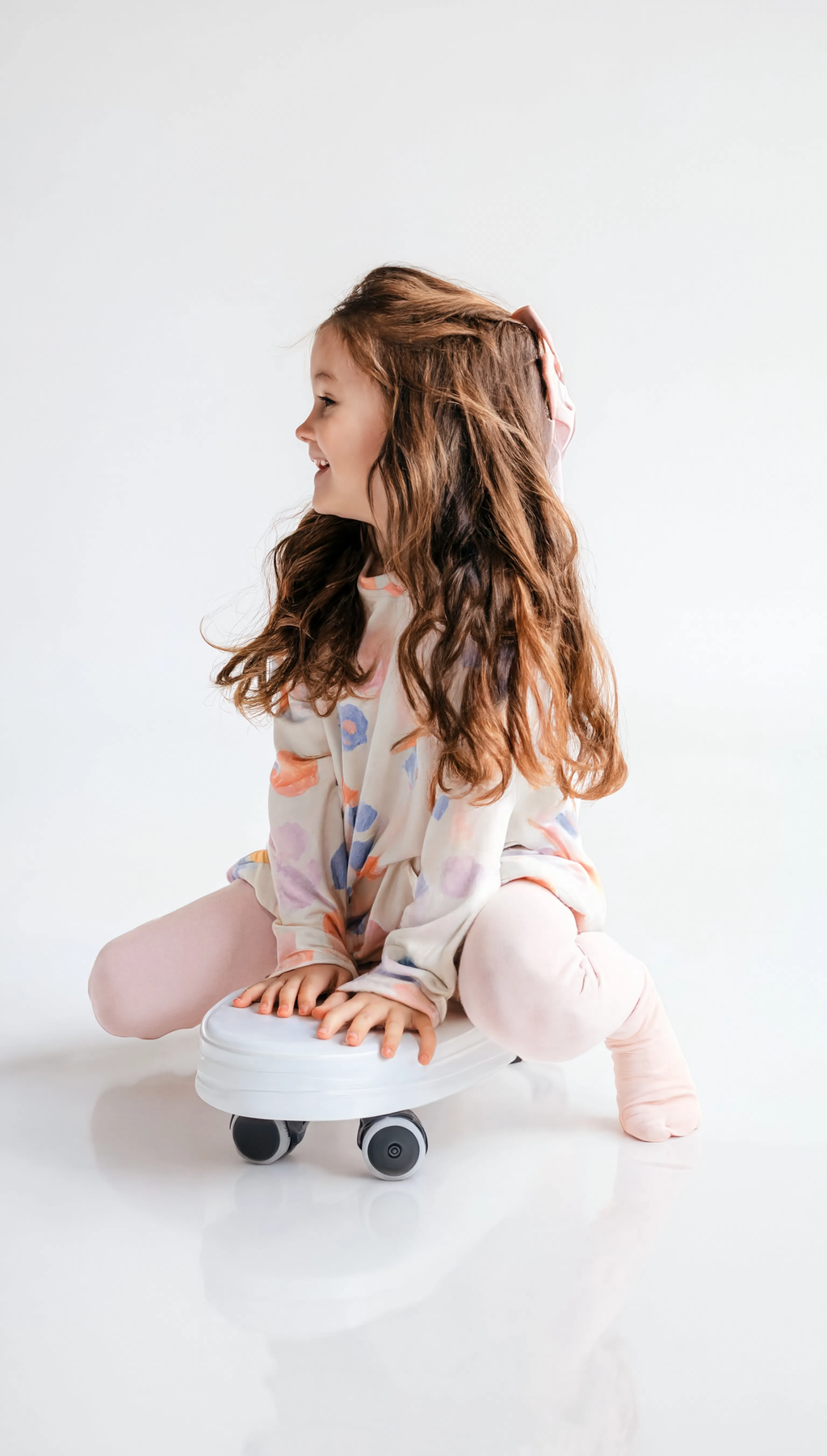 Young girl sitting on a small white scooter with black wheels on a white background