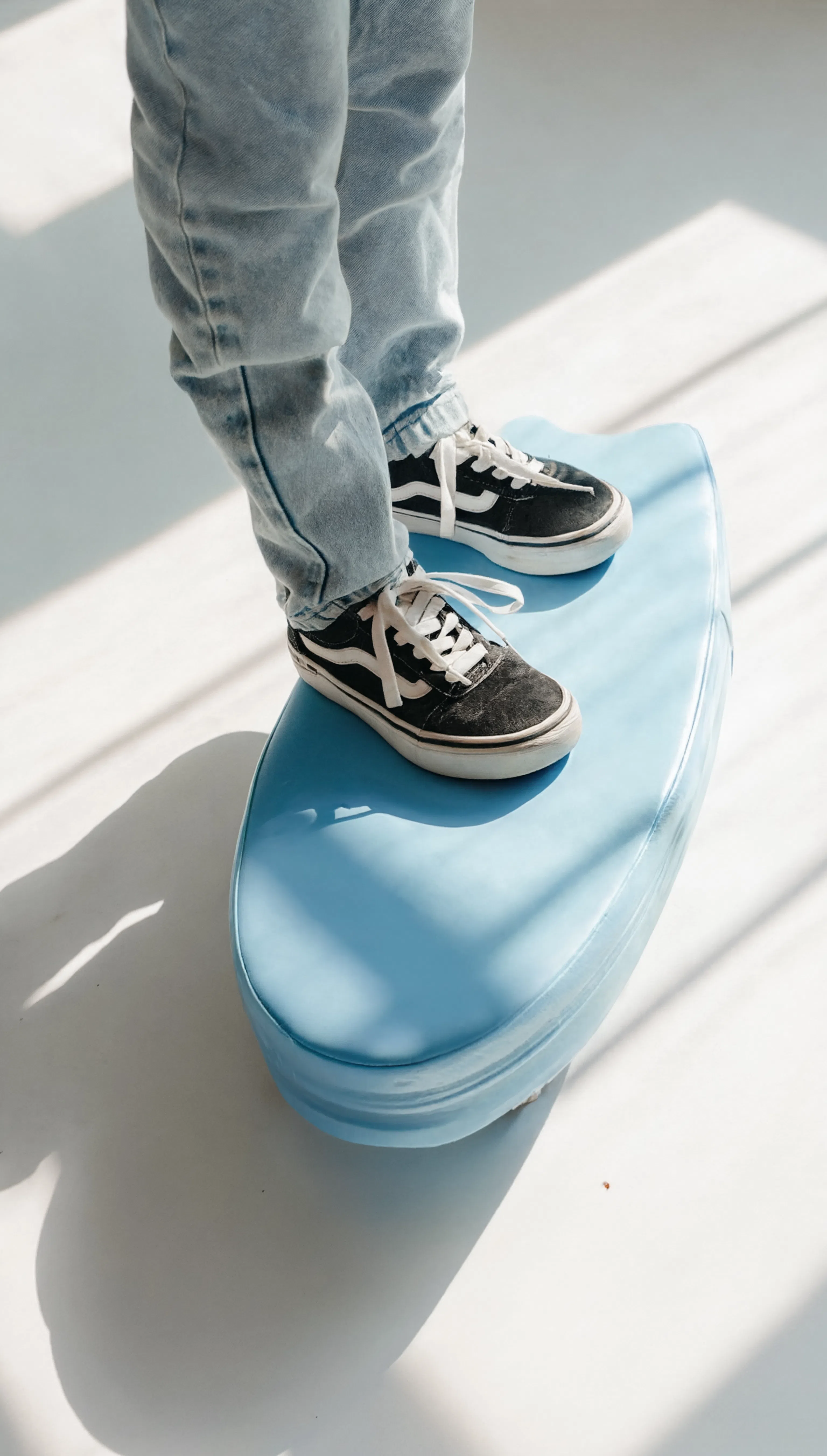 Person wearing black and white sneakers and light blue jeans stepping onto a blue step stool.