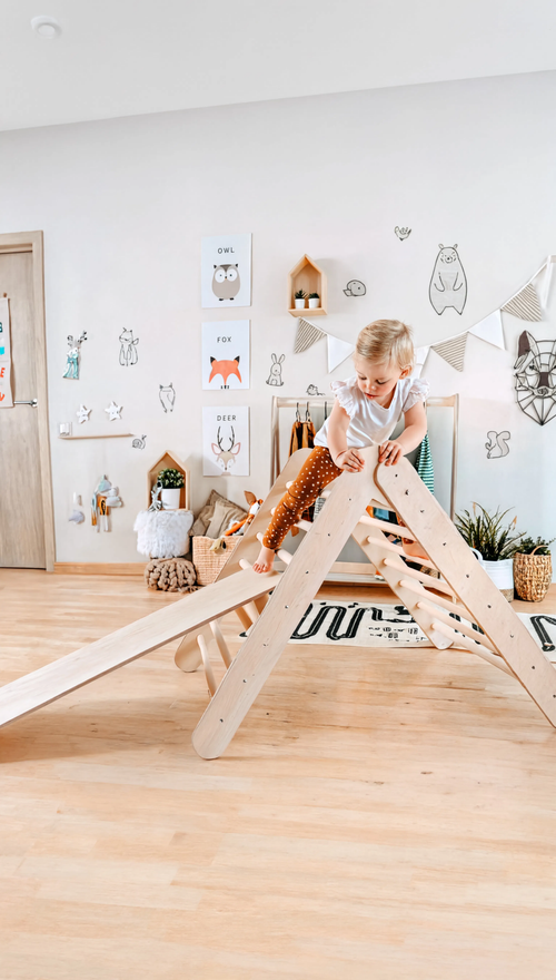 Child playing on a wooden climbing frame in a room with white walls and wooden flooring.
