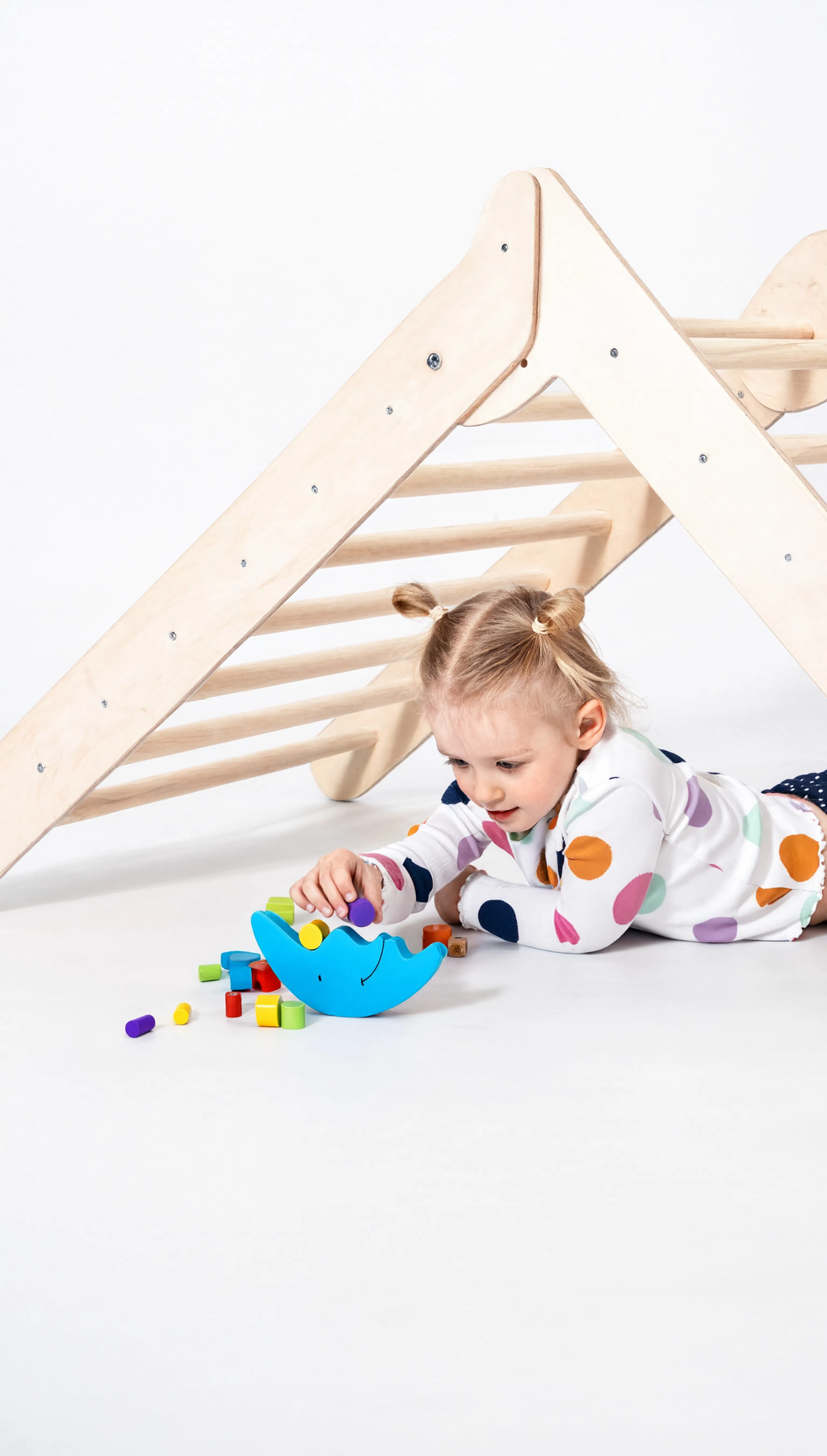 Child playing with colorful toy blocks under a wooden climbing frame.