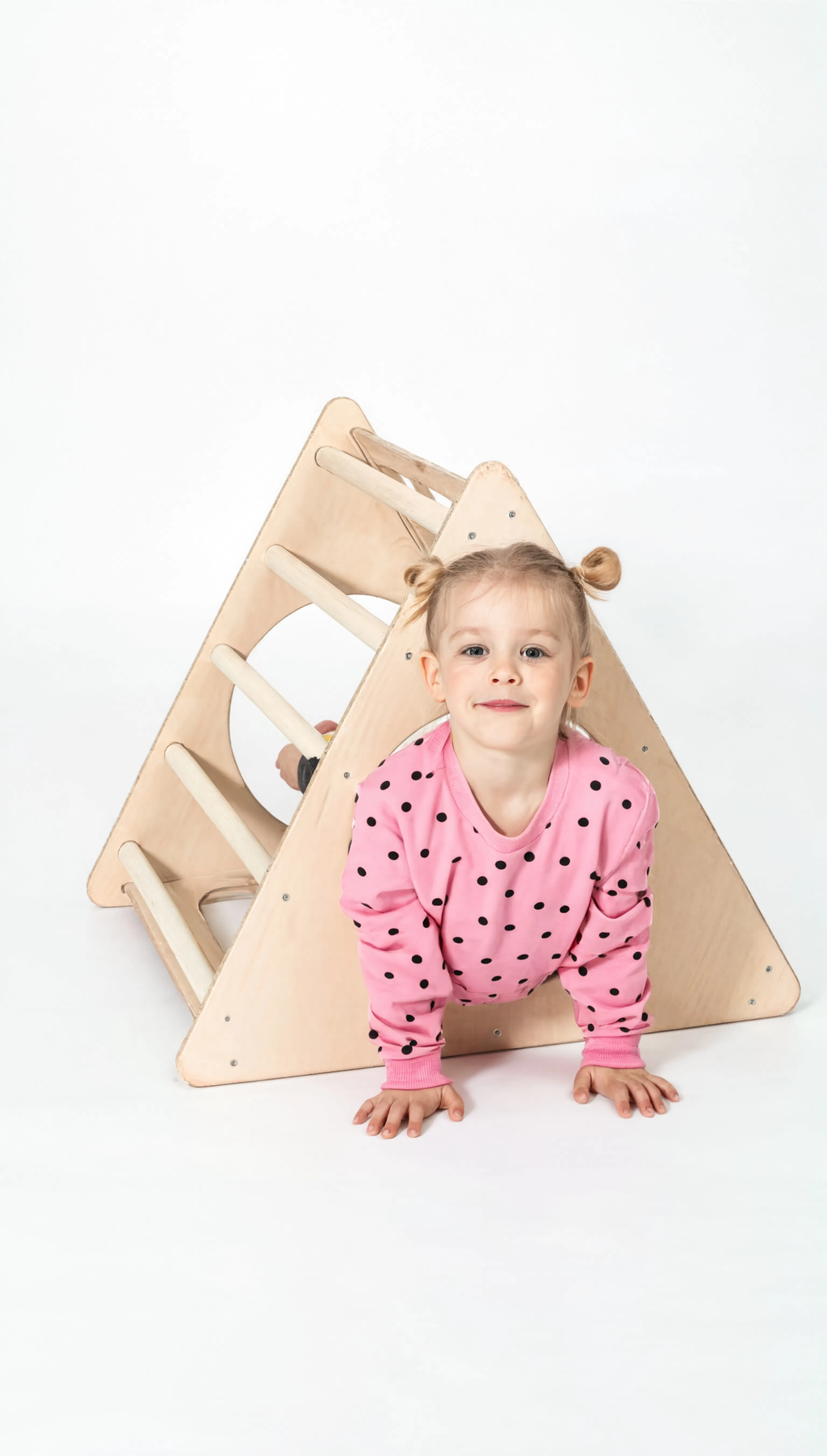 Child in pink outfit standing next to a wooden climbing toy on a white background