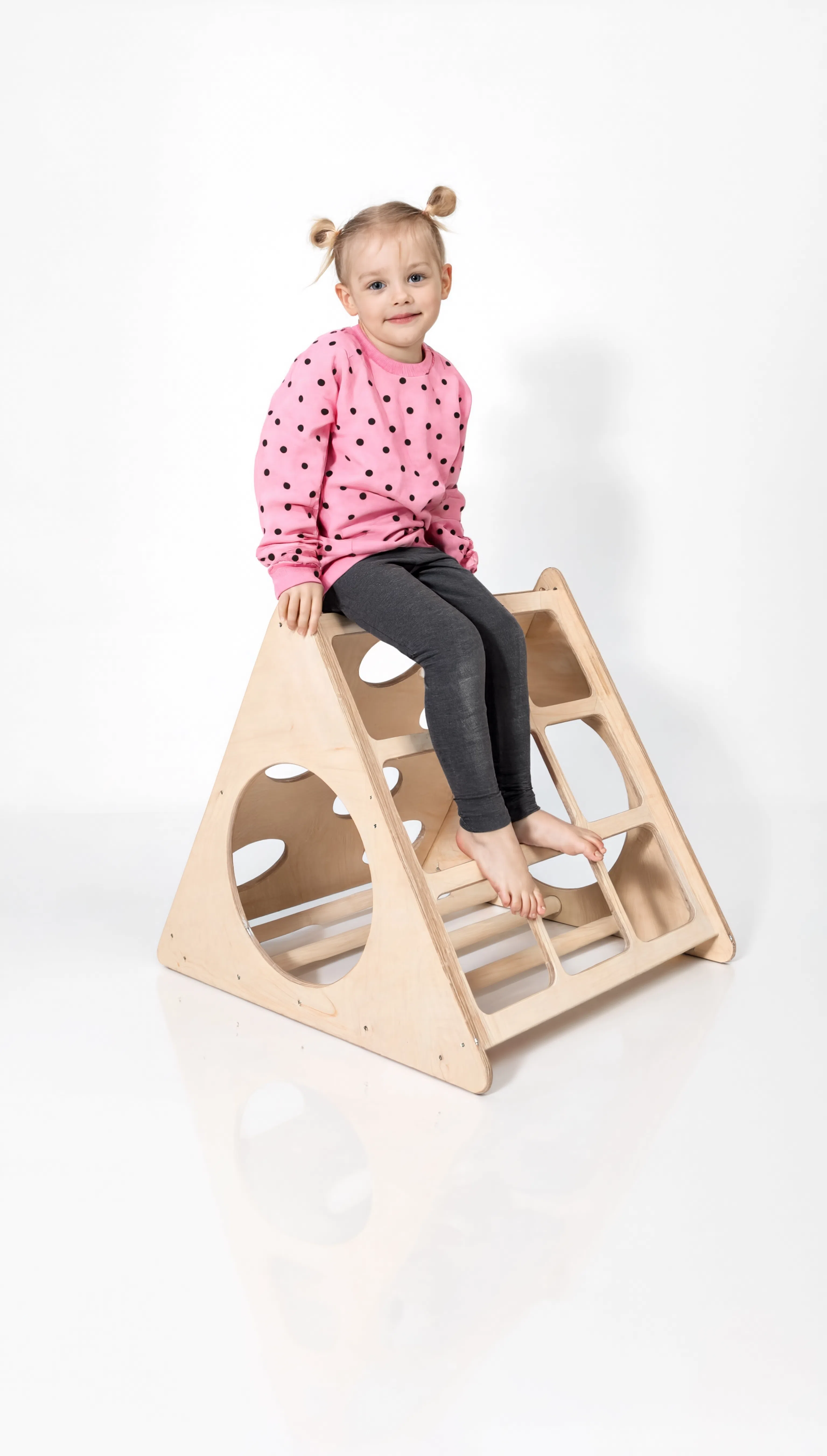 Child sitting on a wooden climbing toy against a white background