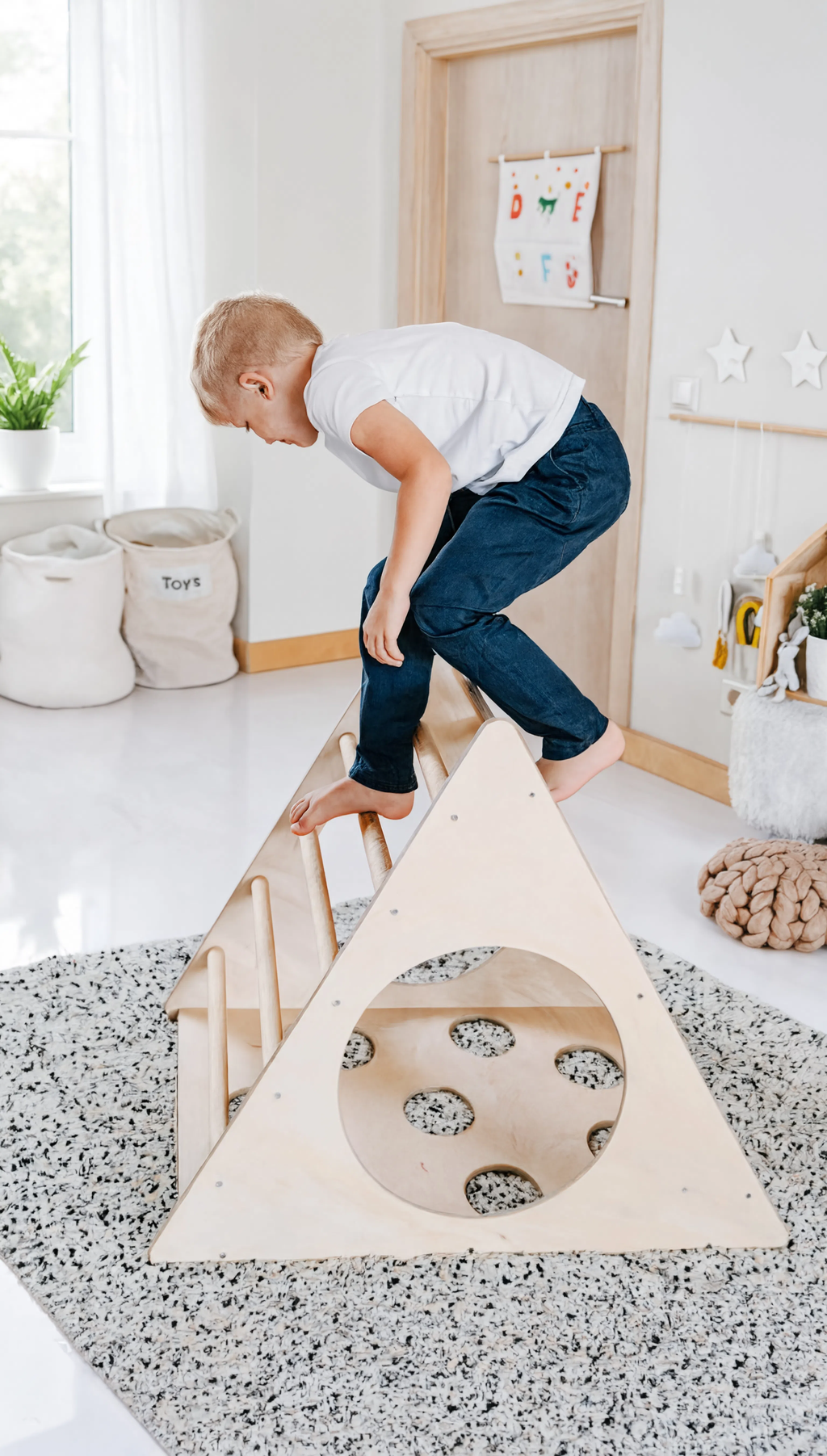 Child playing with a wooden climbing toy in a bright, minimalistic room.