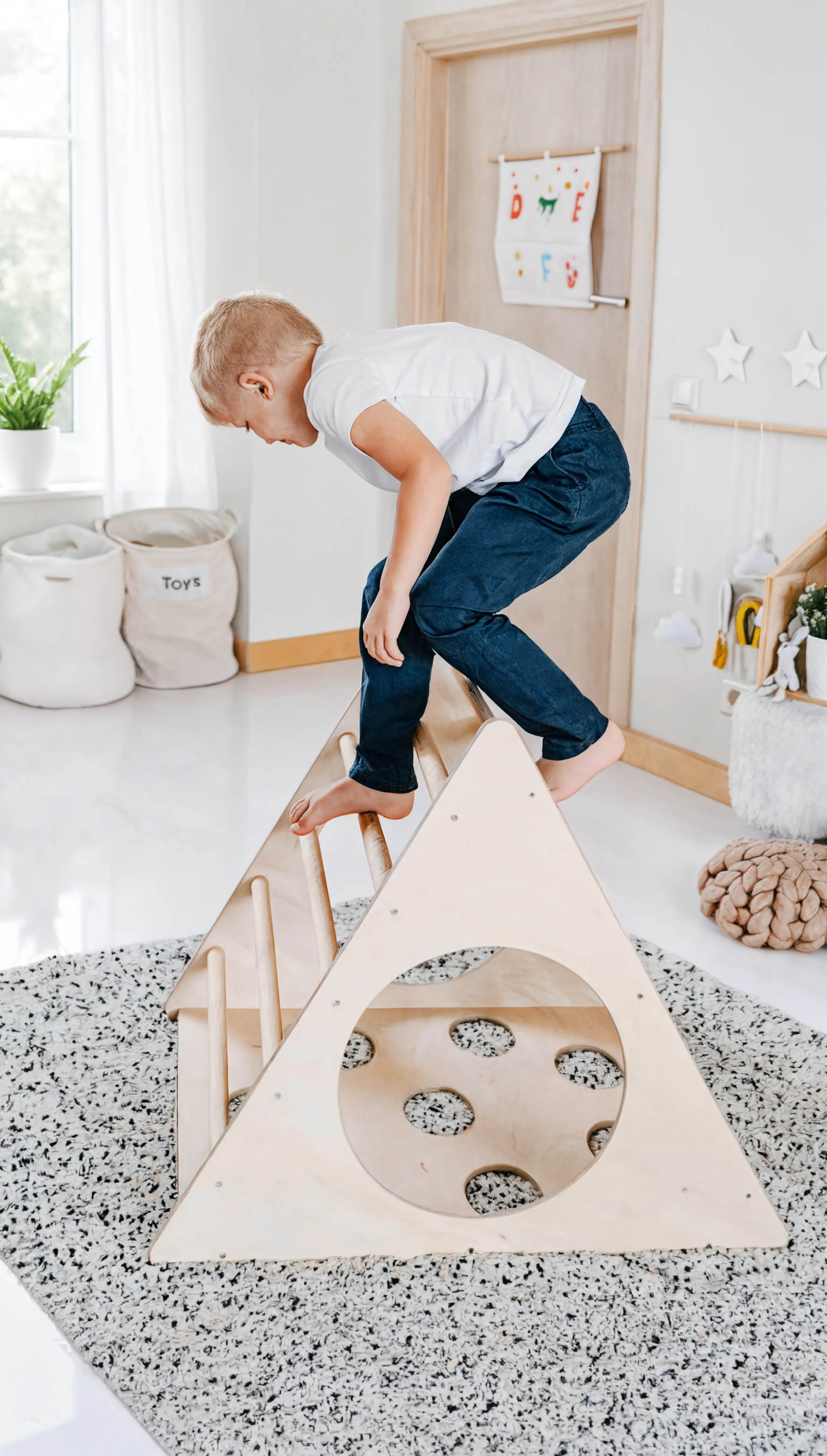 Child playing with a wooden climbing toy in a bright, minimalistic room.