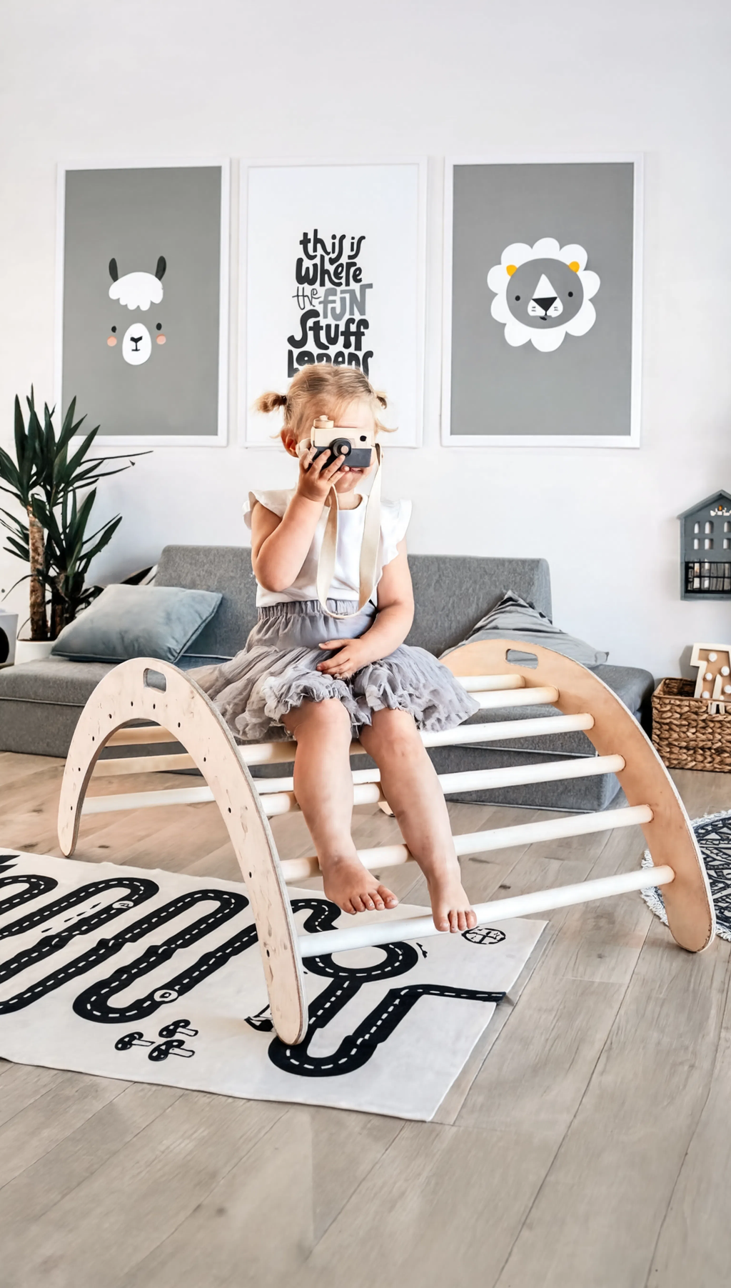 Child sitting on a wooden climbing toy in a room with posters and a rug.