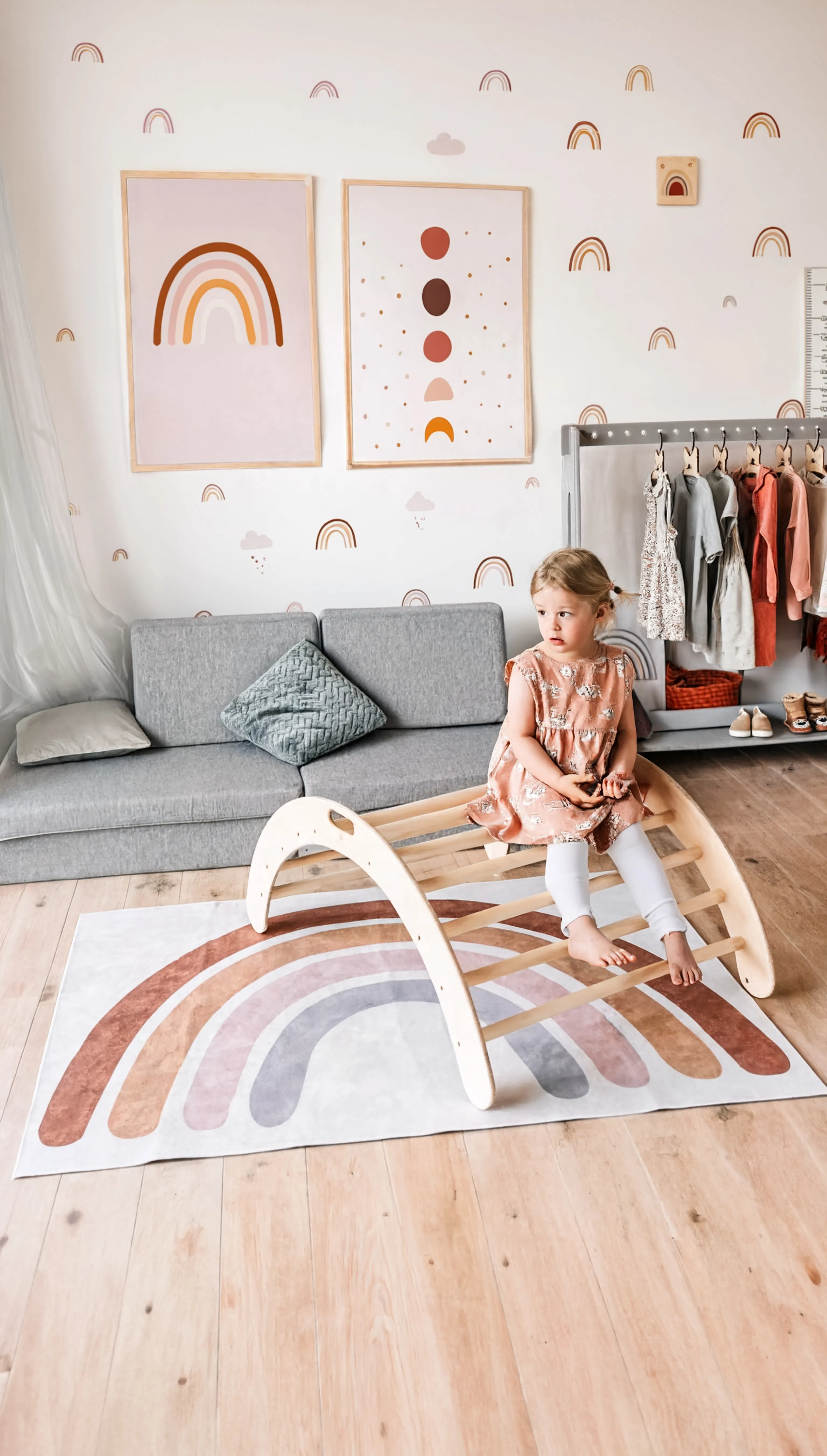 Child playing with a wooden climbing toy on a rainbow-patterned rug in a child-friendly room.