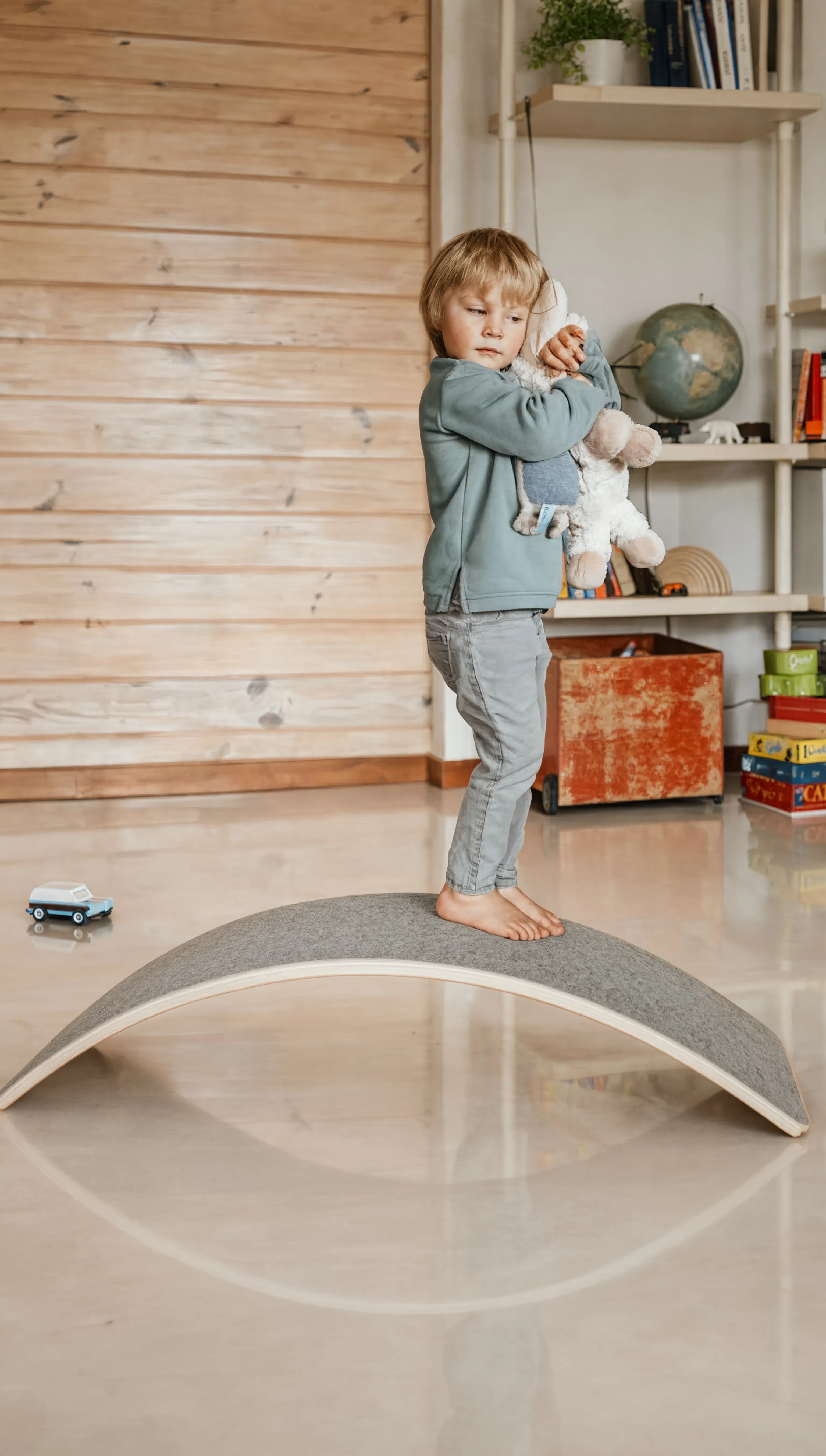 Child playing with a balance board in a room with wooden walls and shelves.