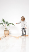 Child standing on a wooden balance beam with a plant in the background