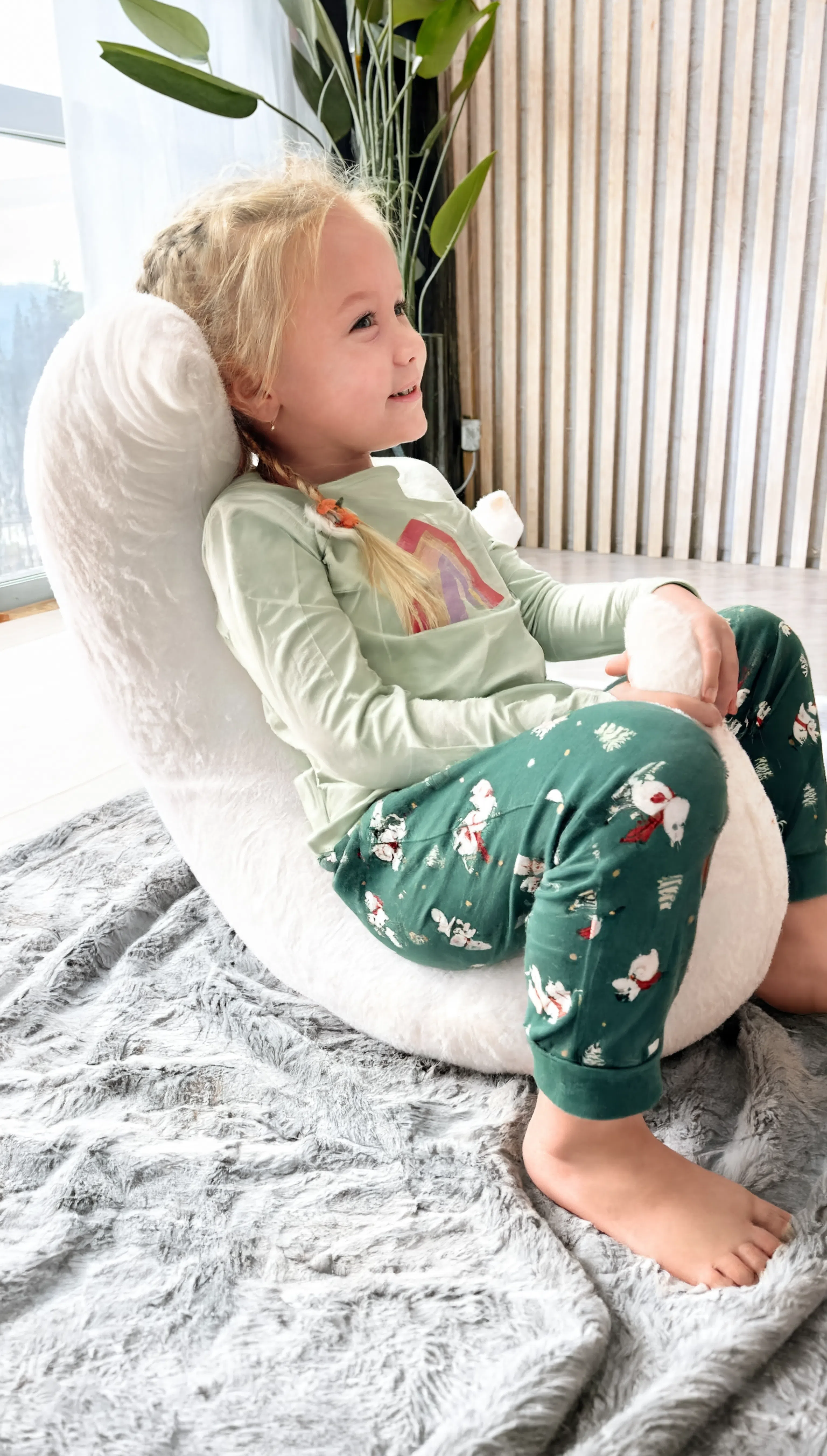 Child sitting on a bean bag chair wearing a light green shirt and dark green pants with animal prints.